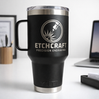 Black travel mug with Etchcraft Precision Engraving logo on a desk with office items.