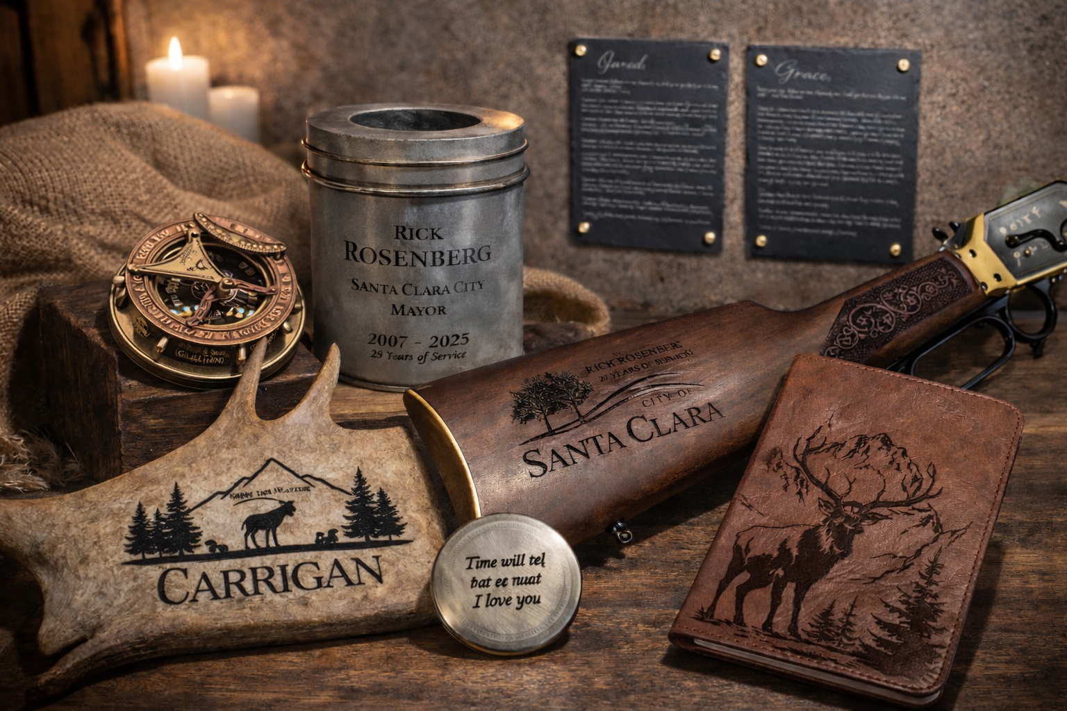 Collection of custom engraved items including a leather journal, rifle stock, antler carving, memorial urn, slate plaques, and metal keepsake displayed on a rustic workbench.