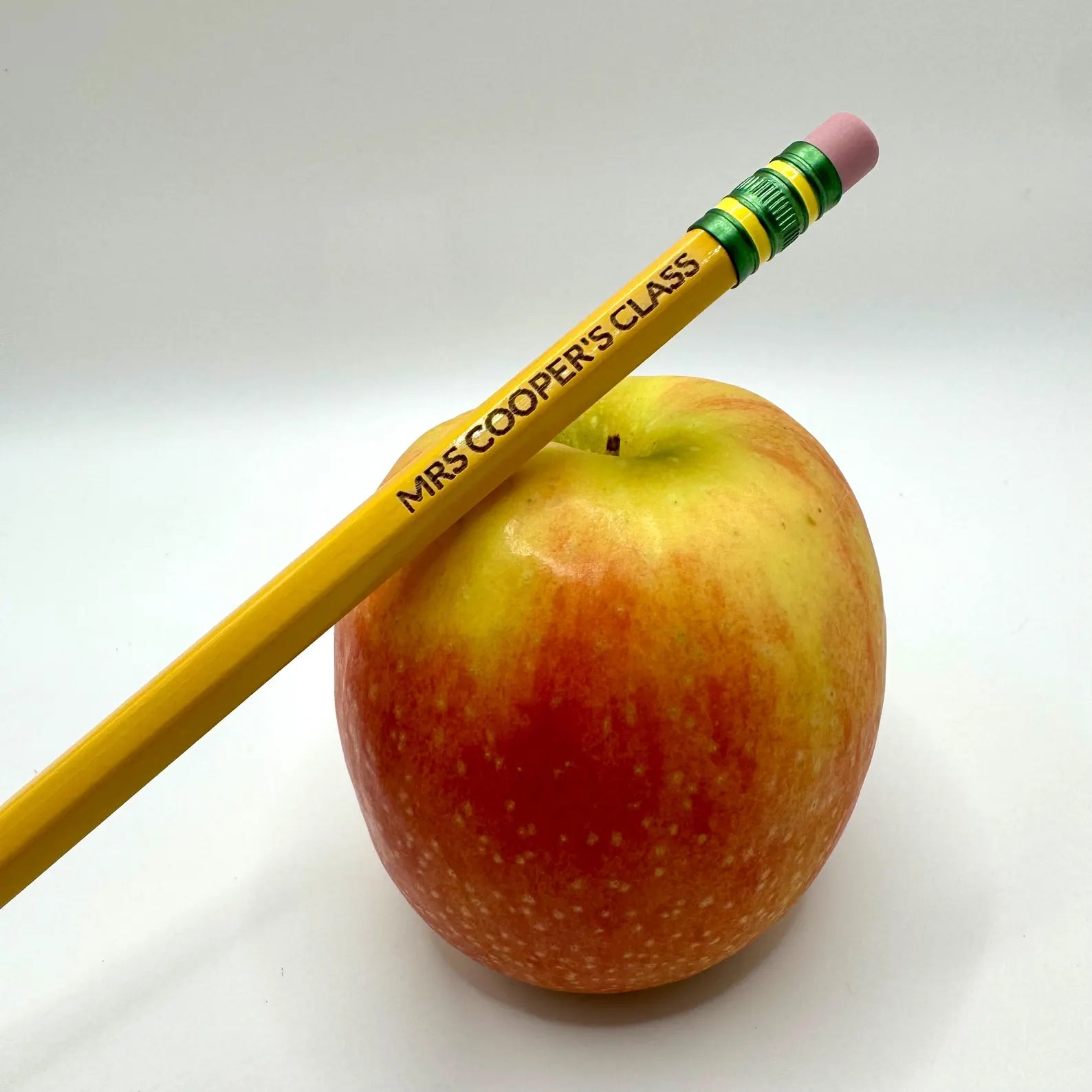 Yellow pencil labeled 'Mrs. Cooper's Class' on a red apple against a white background